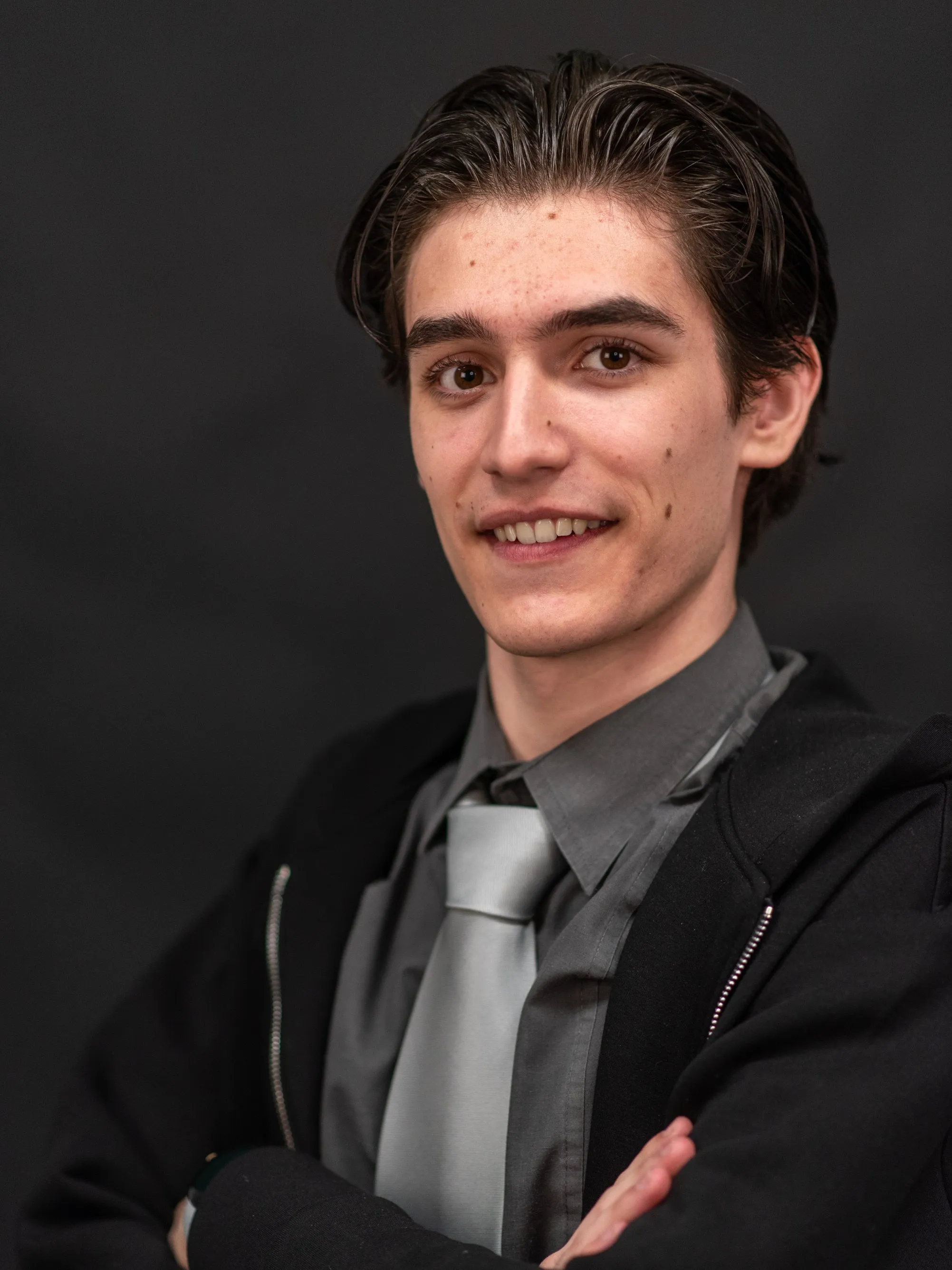 Felix Schneider smiling in a formal gray shirt and silver tie, arms crossed against a dark background.
